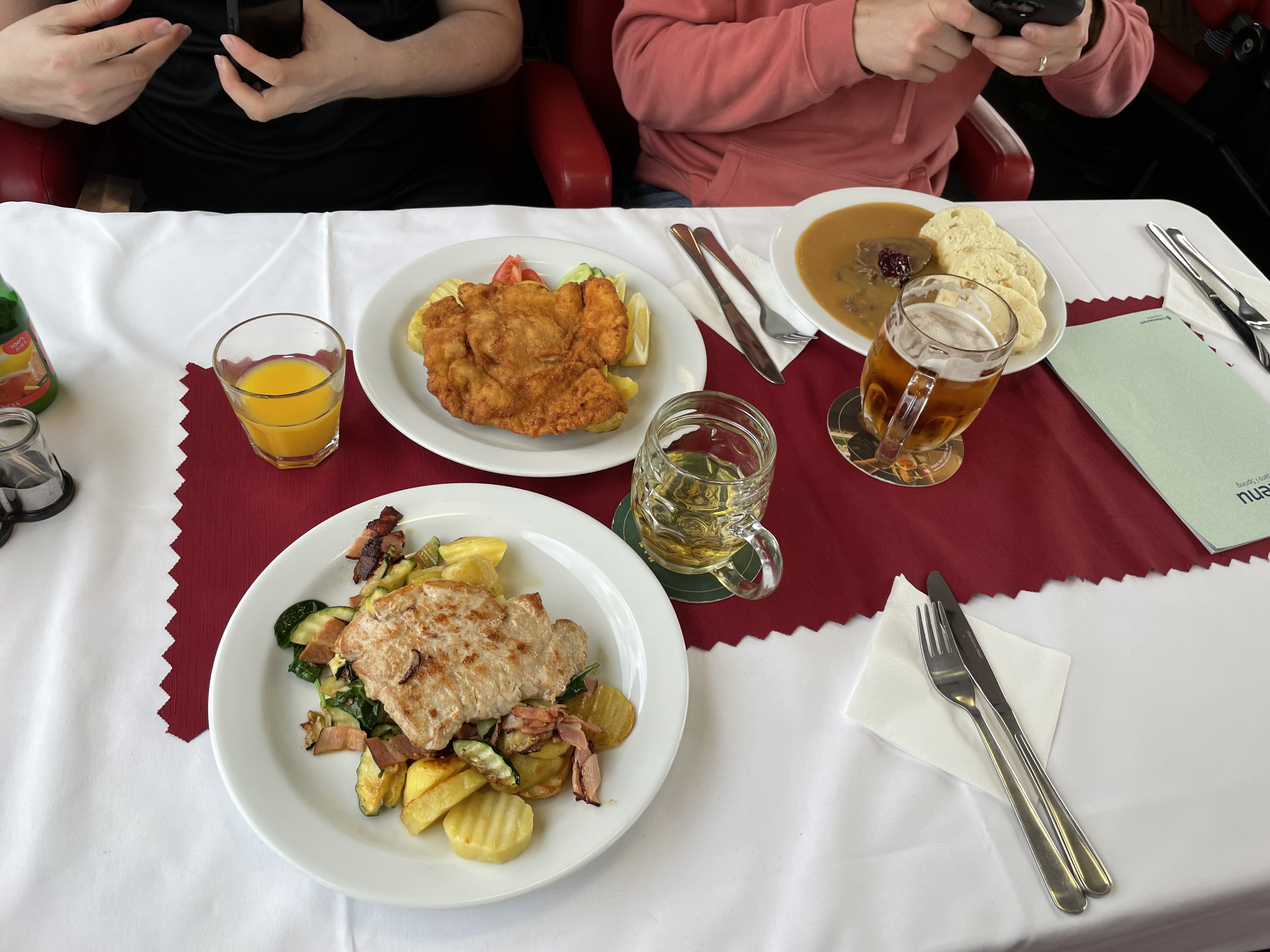 Three plates of food on board a České dráhy restaurant carriage together with an orange juice, a cider and a beer.